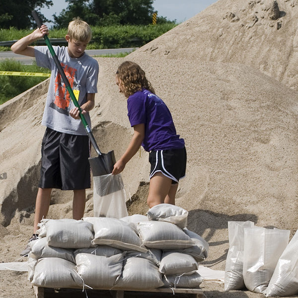 Photo of two kids filling sandbags on a sunny day.